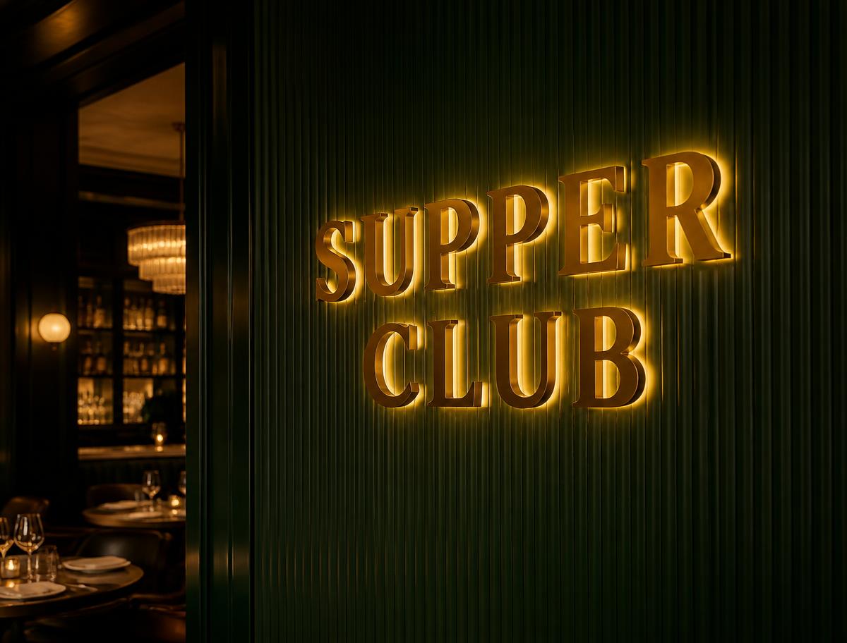 Polished brass halo-lit Supper Club lettering on a fluted green dining room wall